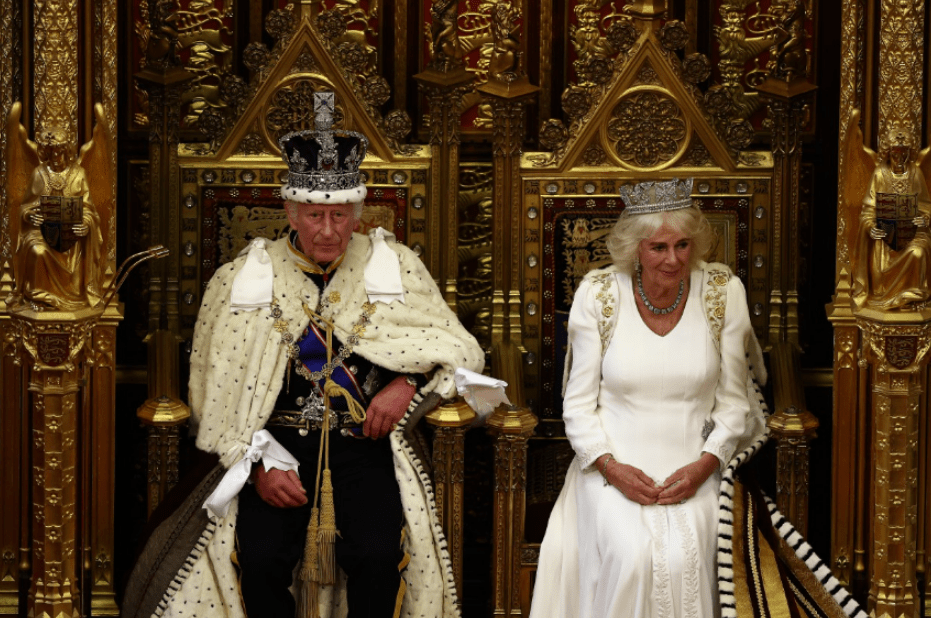 King Charles III, wearing the Imperial State Crown and the Robe of State, sits alongside Queen Camilla during the State Opening of Parliament