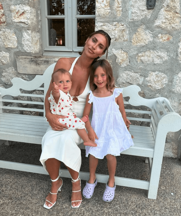 a woman sits on a bench holding two children