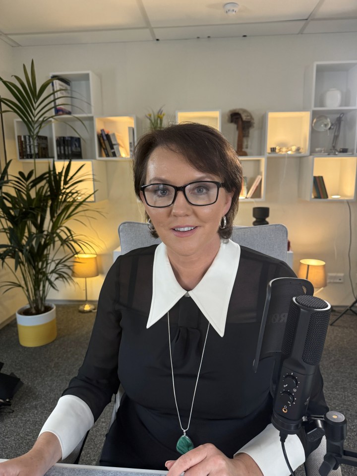 a woman wearing glasses sits in front of a microphone