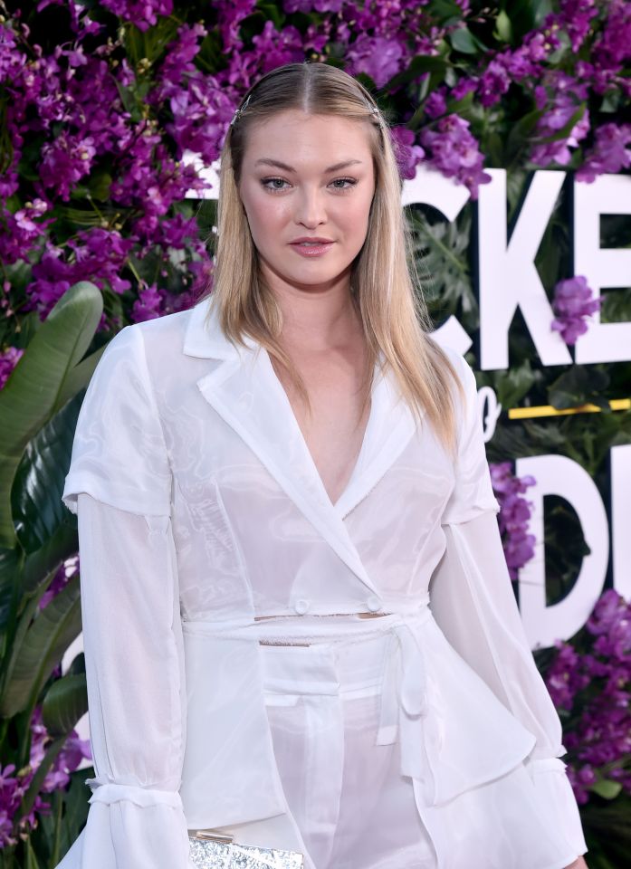 a woman stands in front of purple flowers and a sign that says " cke "