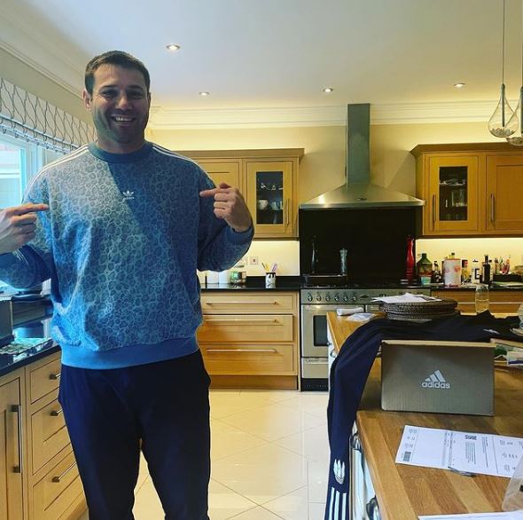 a man in a blue adidas sweatshirt is standing in a kitchen .