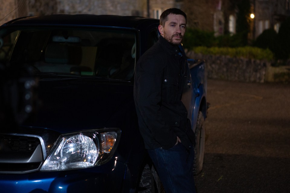 a man leans against a blue truck with his hands in his pockets