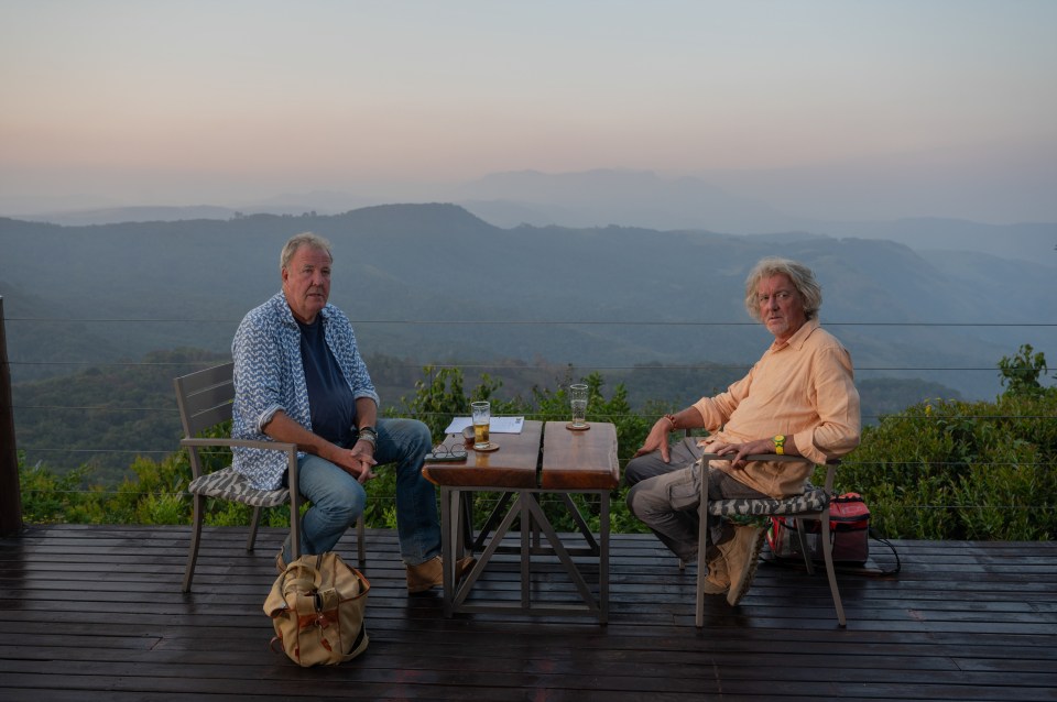 two men sit at a table with mountains in the background