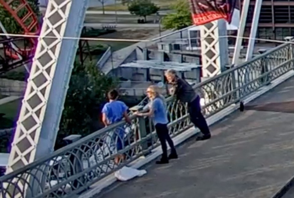 a group of people are standing on a bridge next to a roller coaster .