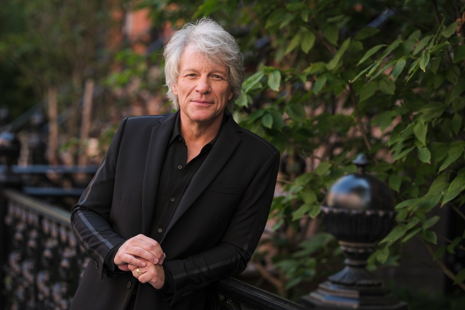 a man in a black suit is leaning against a railing