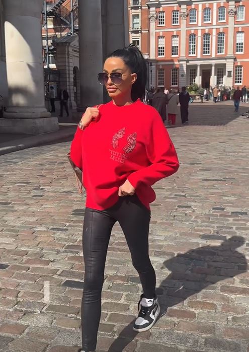 a woman wearing a red sweatshirt and black leggings is walking down a cobblestone street .