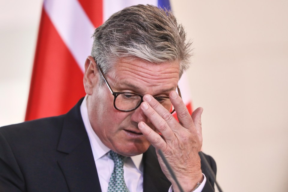 a man wearing glasses wipes his nose with his hand