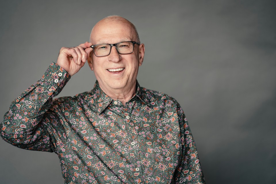 a man wearing glasses and a paisley shirt is smiling