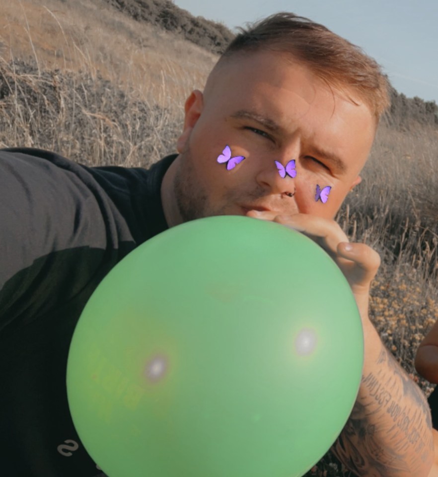 a man blowing up a green balloon with butterflies on his face