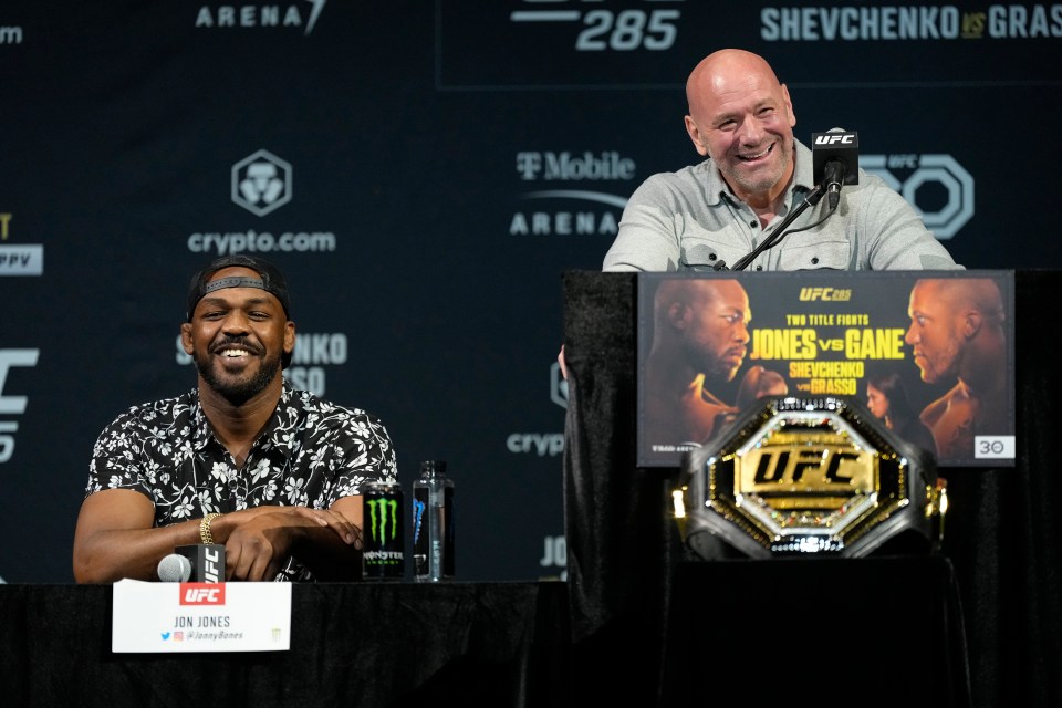 jon jones sits at a table next to dana white