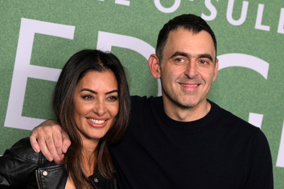 a man and woman are posing for a picture in front of a green background with the letter e on it