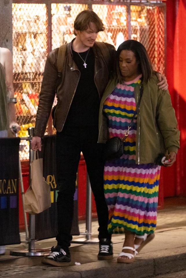 a woman in a rainbow dress is walking with a man in a brown jacket