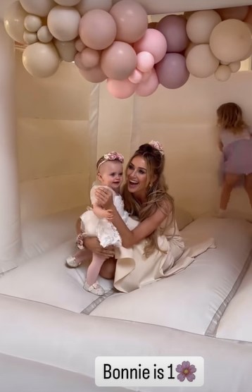 a woman in a white dress is holding a baby in a bouncy house .