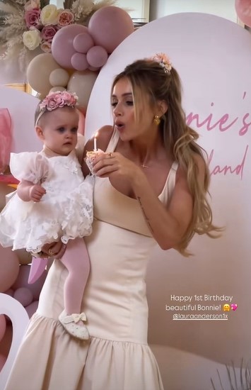 a woman in a white dress is holding a baby and blowing out a candle