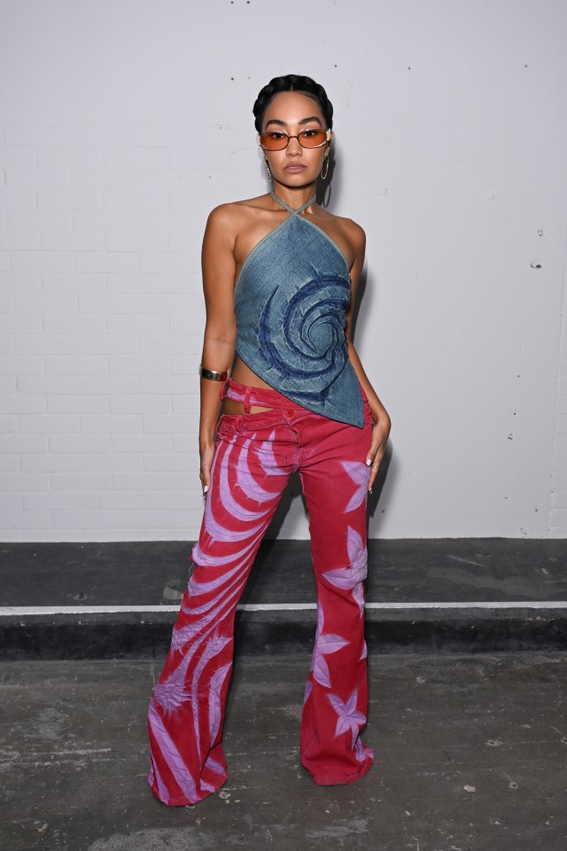 a woman wearing a blue top and red pants stands in front of a white wall