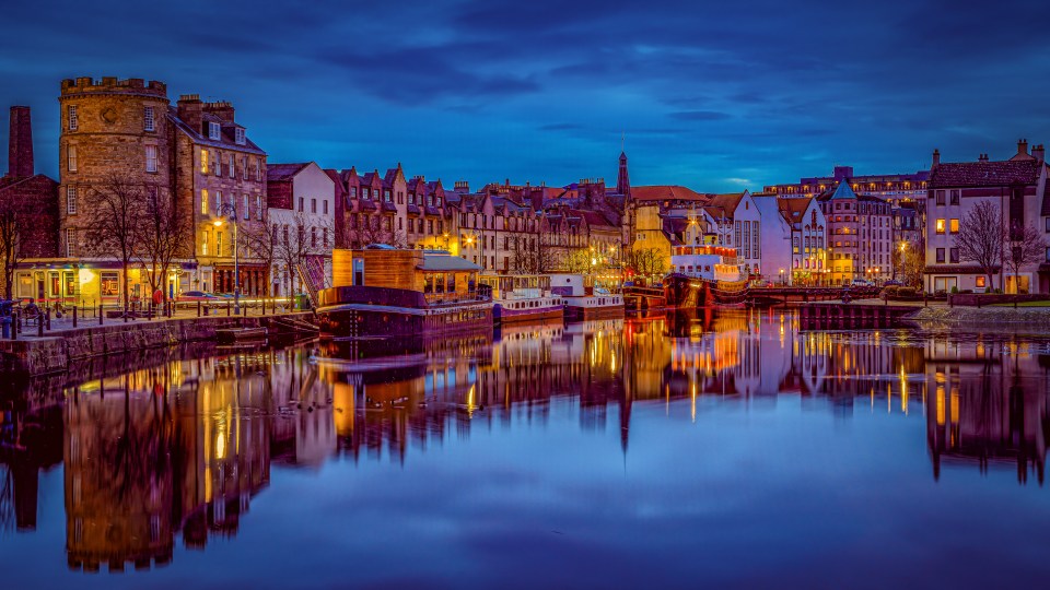 a row of buildings are reflected in a body of water