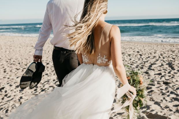 a bride and groom are walking on the beach