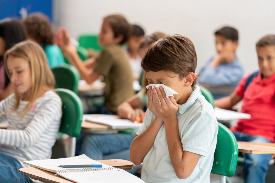 a boy blowing his nose in a classroom with other children