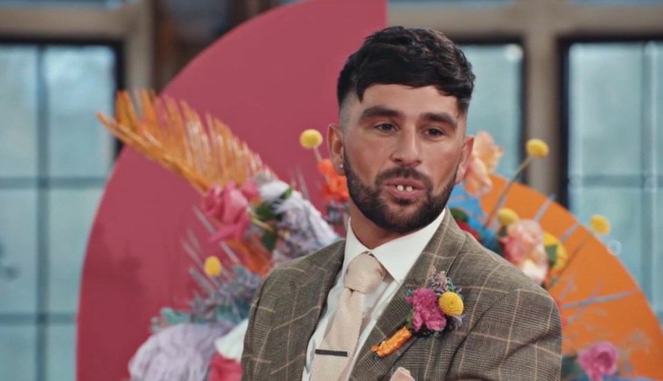 a man in a suit and tie stands in front of flowers