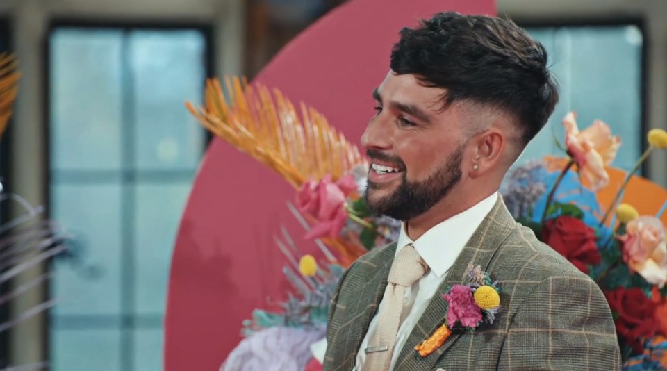 a man in a suit and tie is smiling in front of flowers