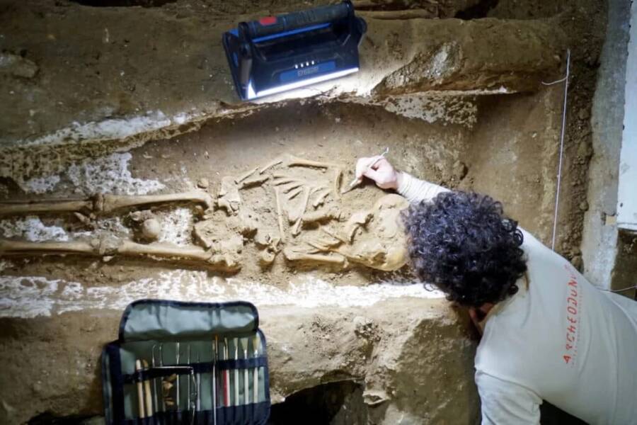 a man wearing a shirt that says archaeology is working on a skeleton