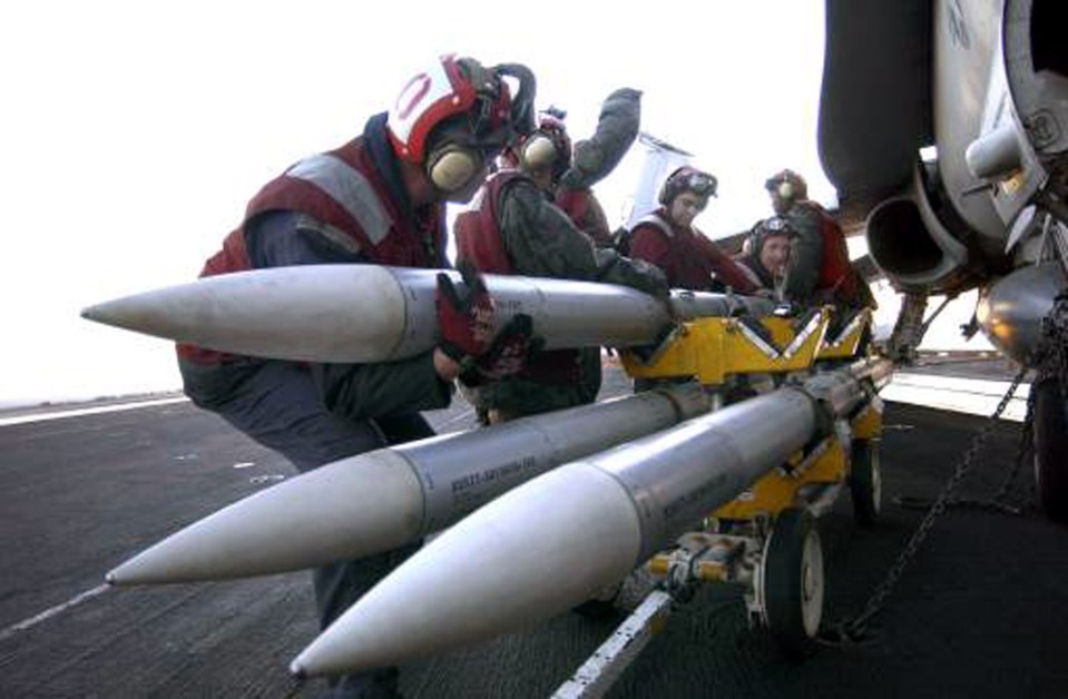 US soldiers manually load an AIM-120 AMRAAM Missile onto an FA-18 Hornet on the flight deck of USS Harry S. Truman