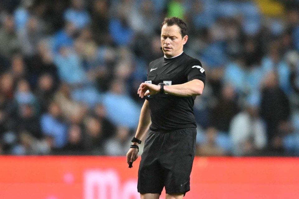 a soccer referee wearing a nike shirt looks at his watch