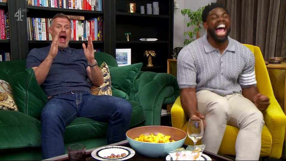 two men are sitting on a couch and one has a bowl of chips in front of him