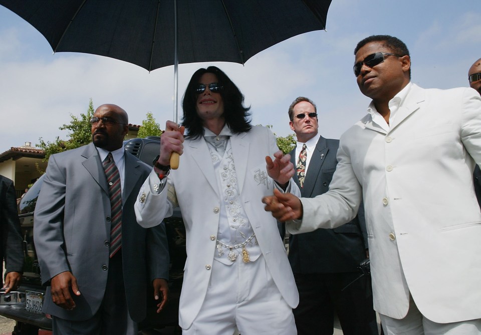 a man in a white suit holds a black umbrella