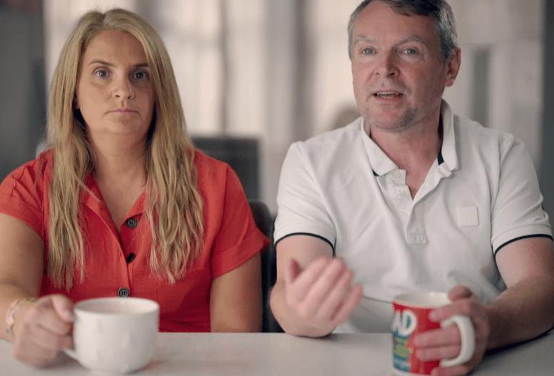 a man and a woman sit at a table with a mug that says ad on it