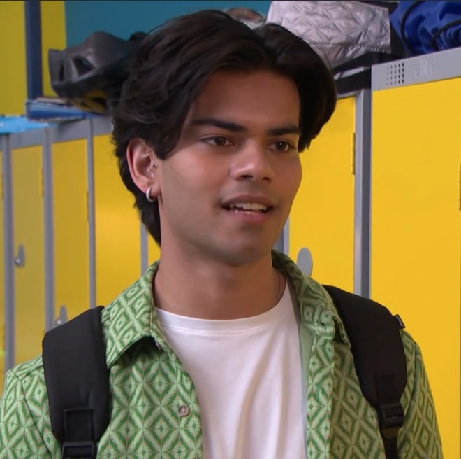 a young man wearing a green shirt and a backpack stands in front of yellow lockers