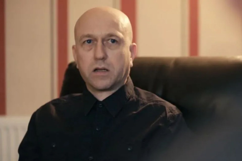 a bald man in a black shirt is sitting in a chair