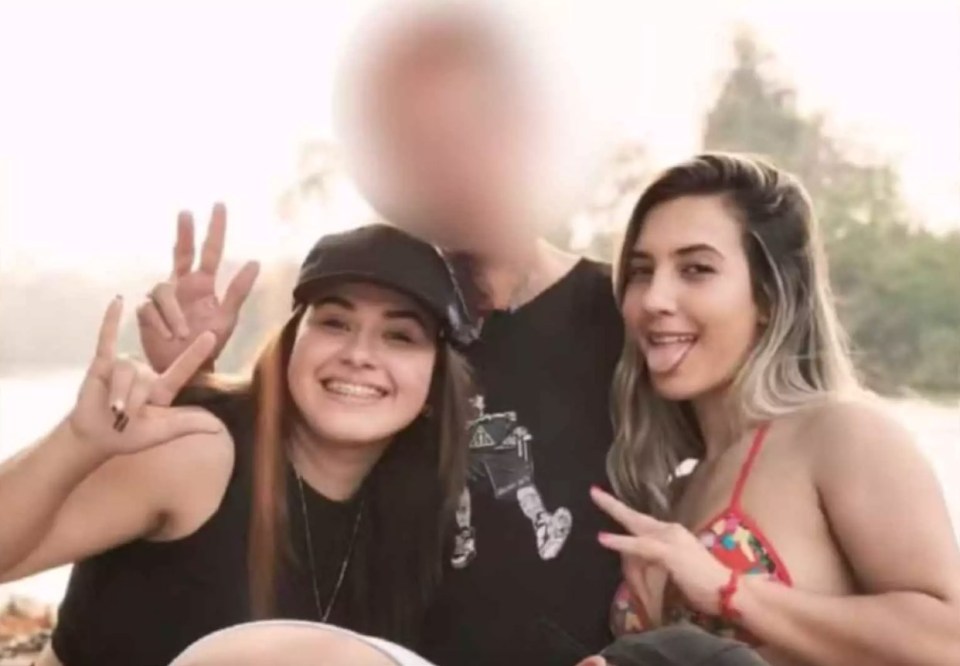 three young women are posing for a picture with a man in the background .