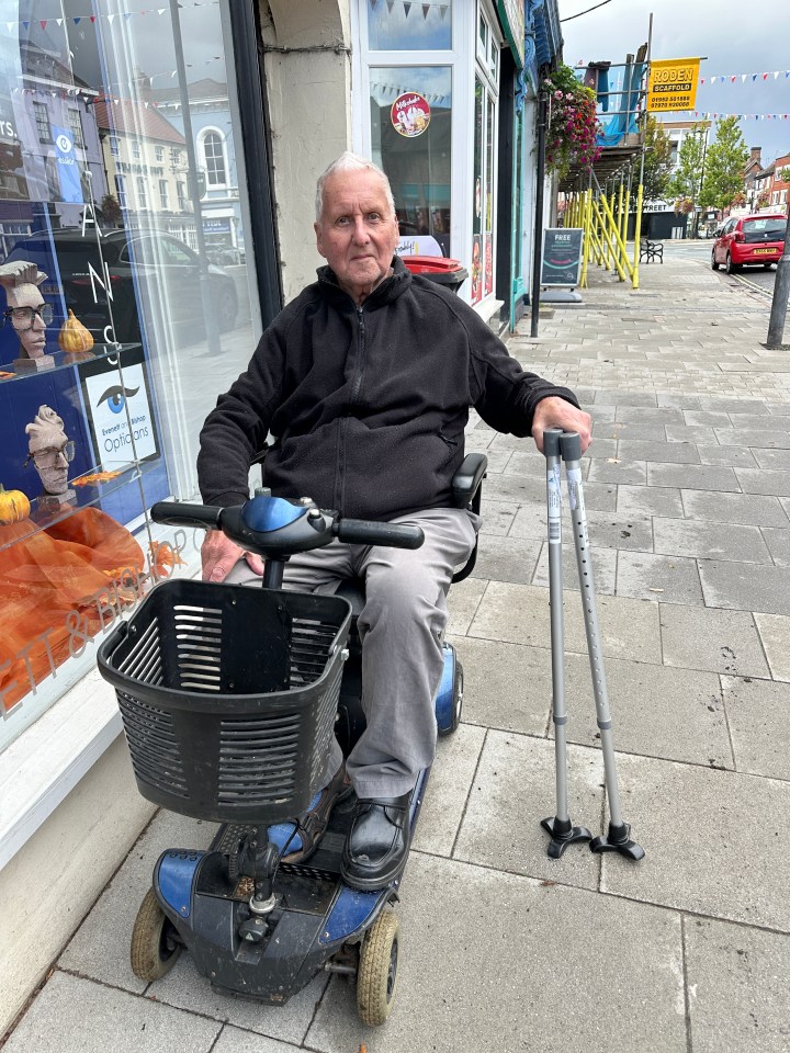 a man sits on a mobility scooter in front of an opticians store