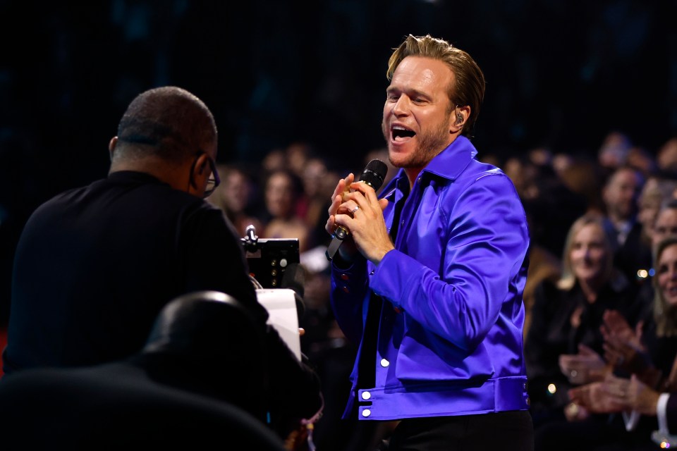 a man in a blue jacket is singing into a microphone