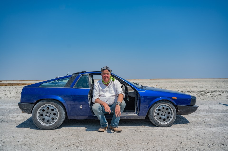 a man sits in the doorway of a blue car