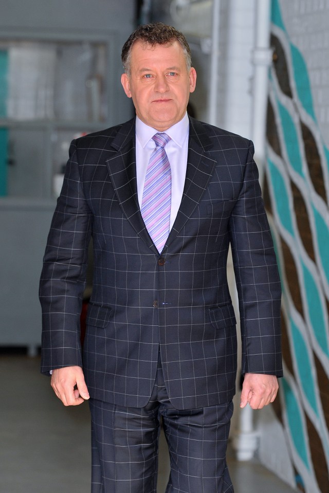 a man in a suit and tie stands in front of a wall