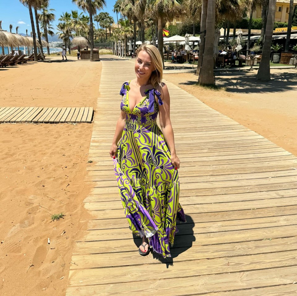 a woman in a green and purple dress stands on a wooden walkway