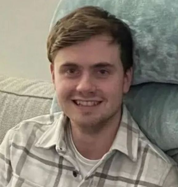 a young man is sitting on a couch wearing a plaid shirt and smiling .