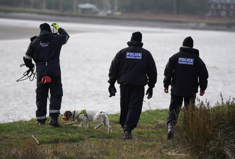 three police officers are walking a dog near a body of water