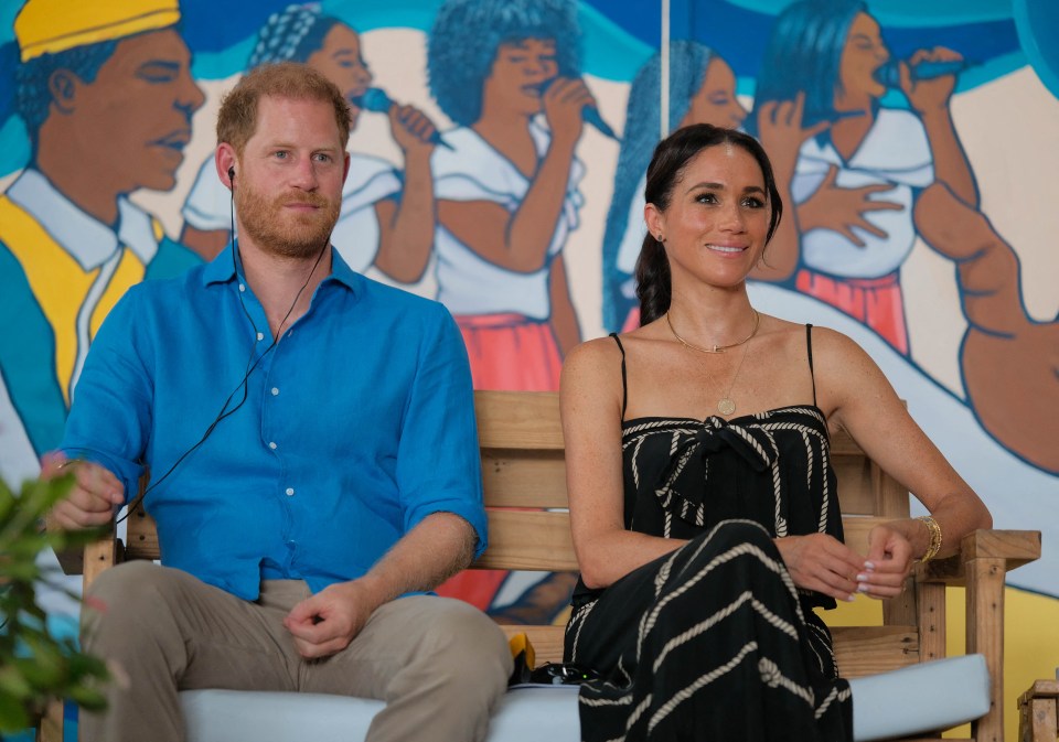 harry and meghan sit on a bench in front of a painting