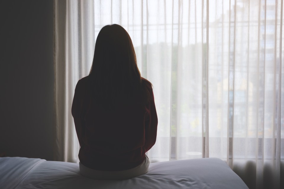 a woman sits on a bed looking out a window