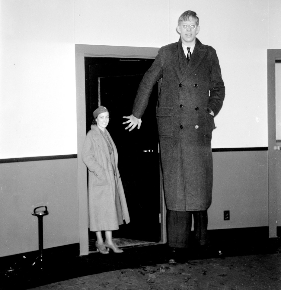 a woman stands next to a very tall man in a coat