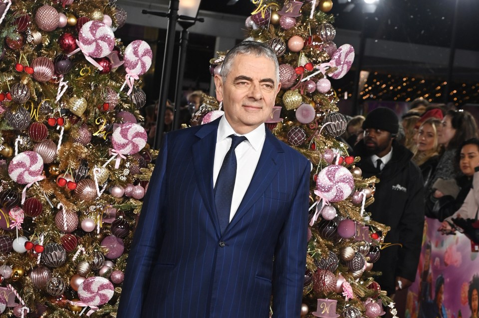 a man in a suit and tie stands in front of a christmas tree