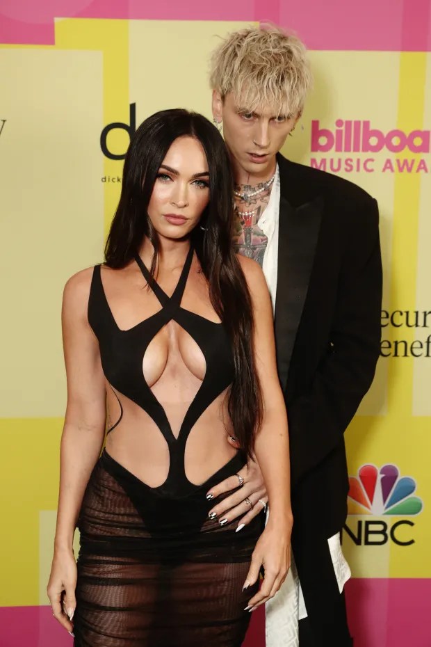 a man and a woman pose on a red carpet in front of a billboard music awards sign