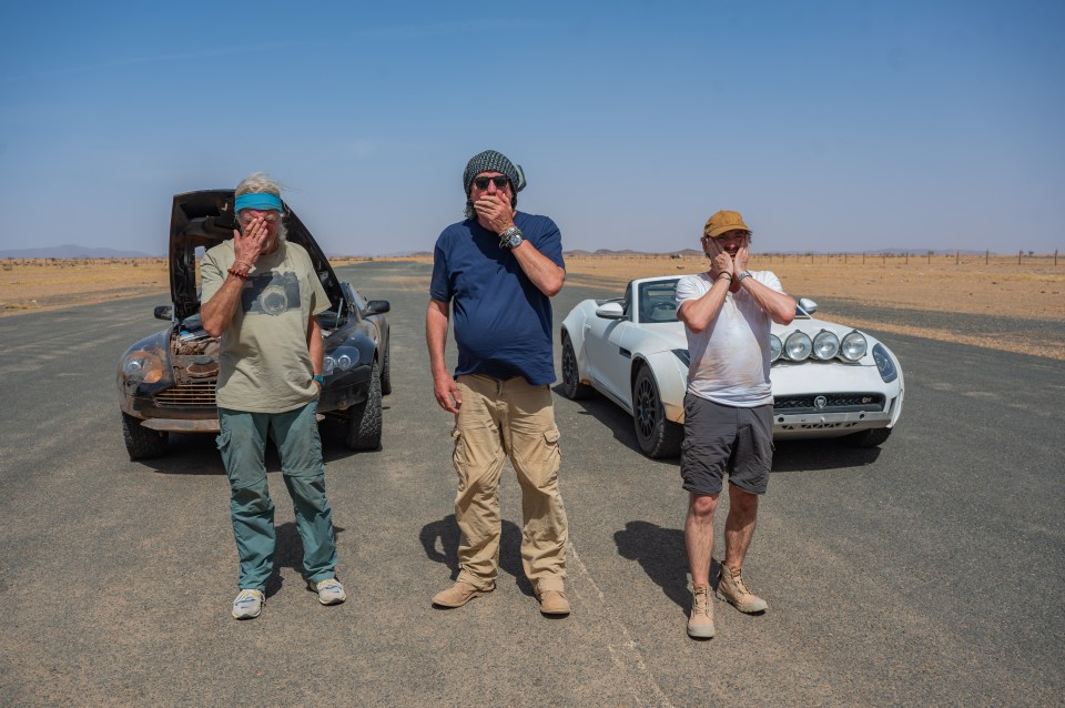 three men covering their faces with their hands in front of two cars