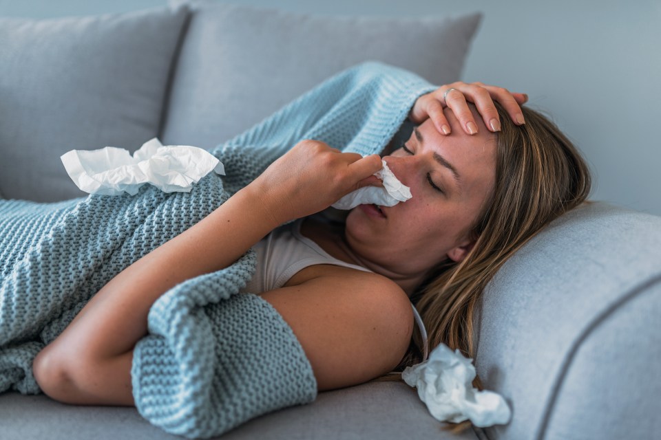 a woman laying on a couch blowing her nose with a napkin