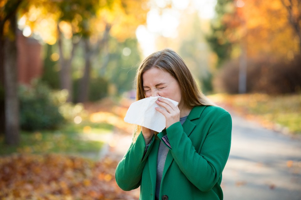 a woman in a green coat blows her nose into a napkin