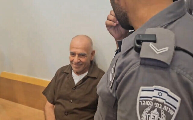 a man in a brown shirt is sitting in a courtroom next to a police officer .