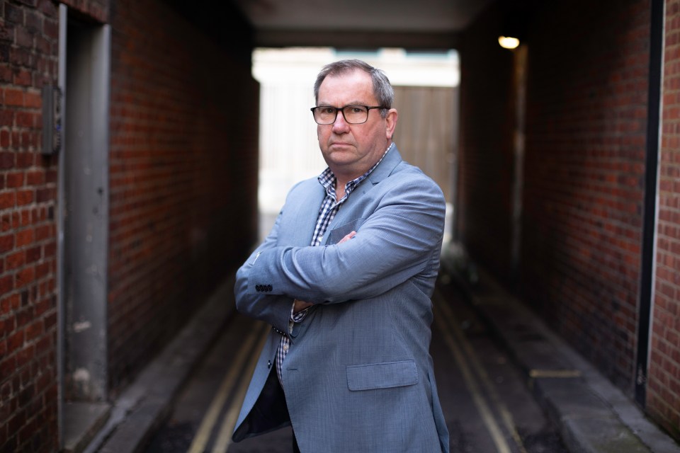 a man in a suit and glasses stands with his arms crossed